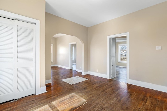 spare room featuring arched walkways, wood finished floors, and baseboards