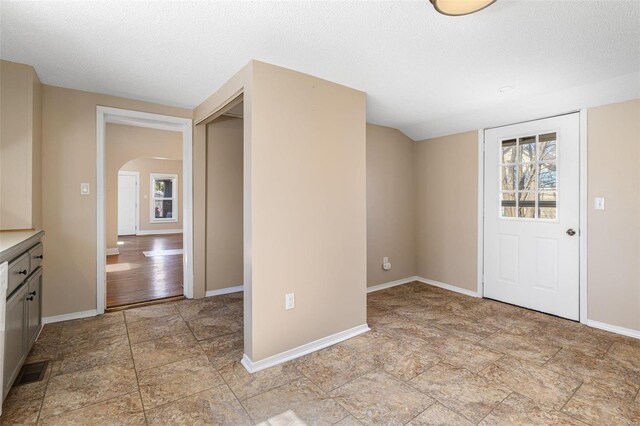 foyer with baseboards, arched walkways, and a textured ceiling