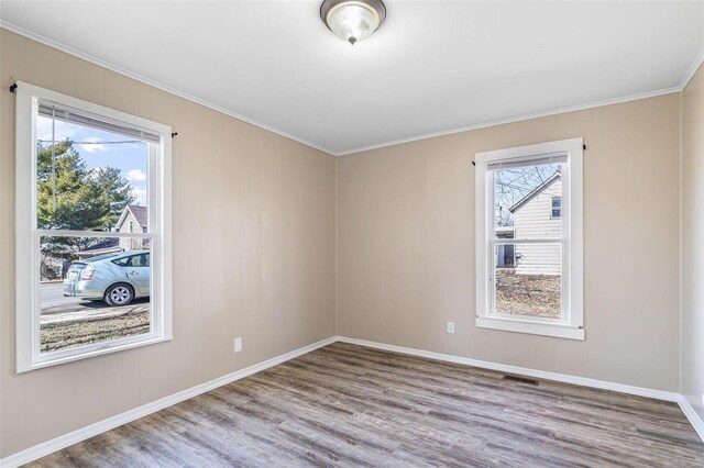 empty room with ornamental molding, plenty of natural light, wood finished floors, and baseboards