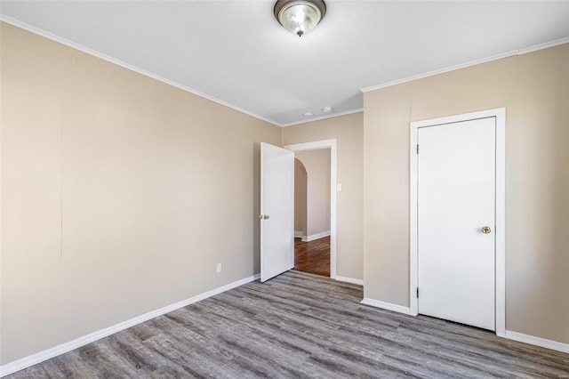 unfurnished bedroom with baseboards, arched walkways, wood finished floors, and ornamental molding