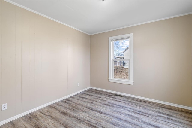 empty room with baseboards, wood finished floors, visible vents, and crown molding