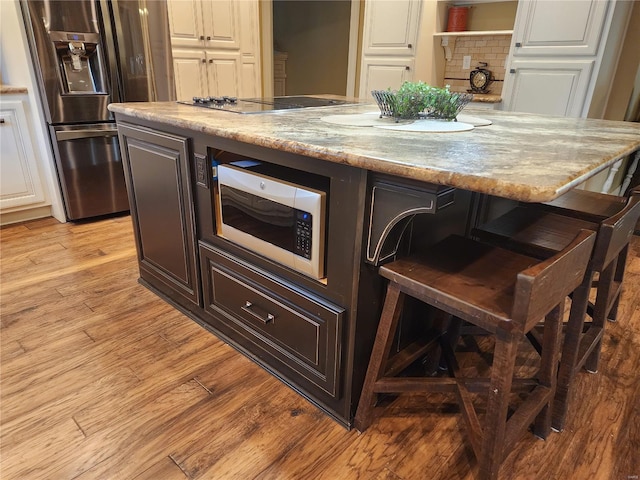 kitchen with dark brown cabinetry, white microwave, light wood-type flooring, and stainless steel fridge with ice dispenser