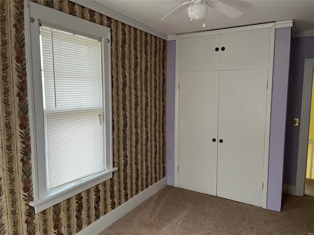 unfurnished bedroom with ceiling fan, carpet floors, crown molding, and a closet