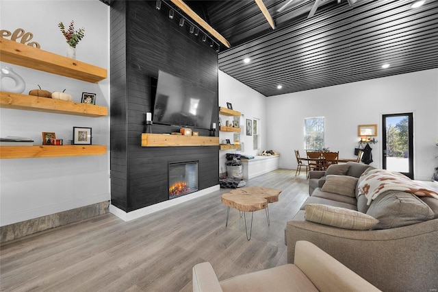 living room featuring a towering ceiling, a fireplace, track lighting, and light wood-type flooring