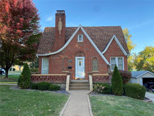 tudor-style house featuring an outdoor structure, a front yard, and a garage