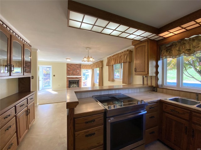 kitchen with kitchen peninsula, stainless steel electric range, sink, and a brick fireplace