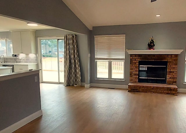 unfurnished living room with light wood-type flooring, vaulted ceiling, and a brick fireplace