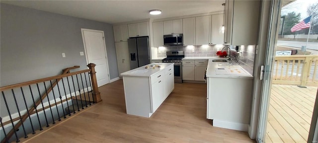 kitchen with appliances with stainless steel finishes, sink, light hardwood / wood-style flooring, white cabinets, and a center island