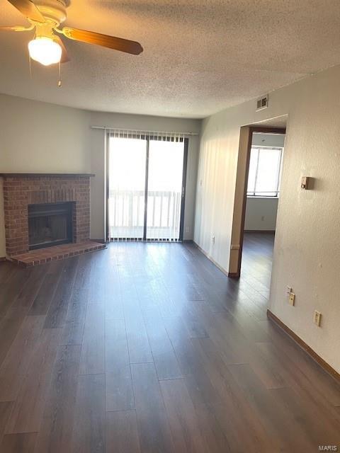 unfurnished living room featuring dark wood-type flooring, ceiling fan, a textured ceiling, and a fireplace