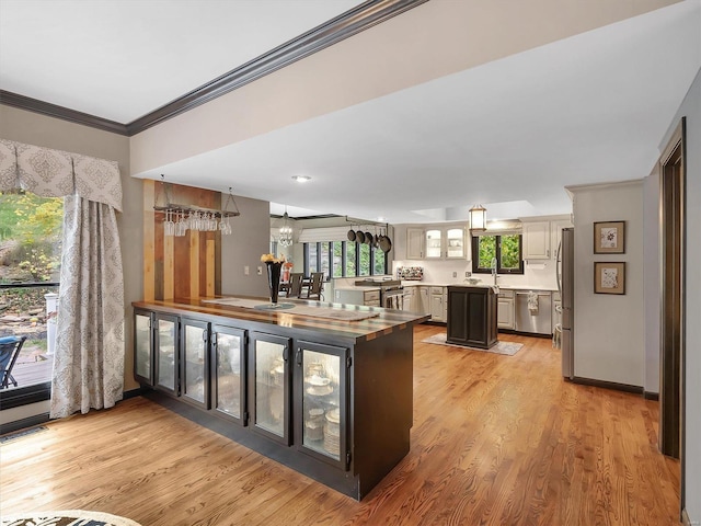 kitchen with sink, kitchen peninsula, stainless steel appliances, ornamental molding, and light hardwood / wood-style flooring