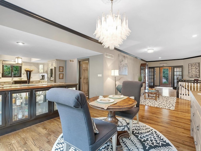 dining room with light hardwood / wood-style floors, a notable chandelier, ornamental molding, and french doors