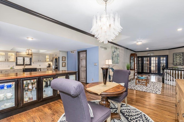 dining room featuring wood-type flooring, ornamental molding, a chandelier, and french doors