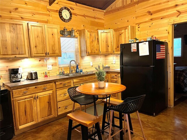 kitchen featuring lofted ceiling, wooden walls, sink, and black fridge