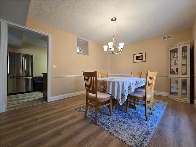 dining space with a notable chandelier, a textured ceiling, and dark hardwood / wood-style flooring