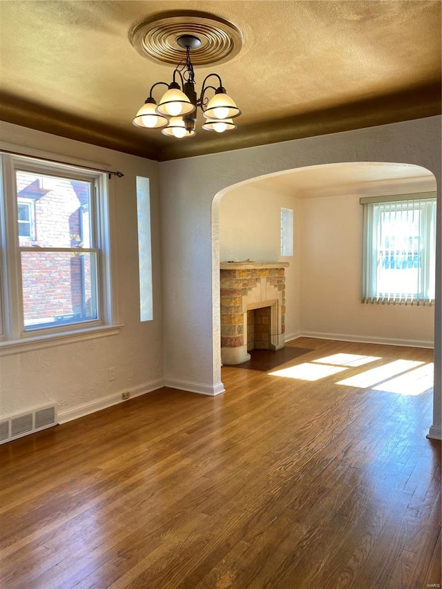 unfurnished living room with a fireplace, a textured ceiling, hardwood / wood-style flooring, and a notable chandelier