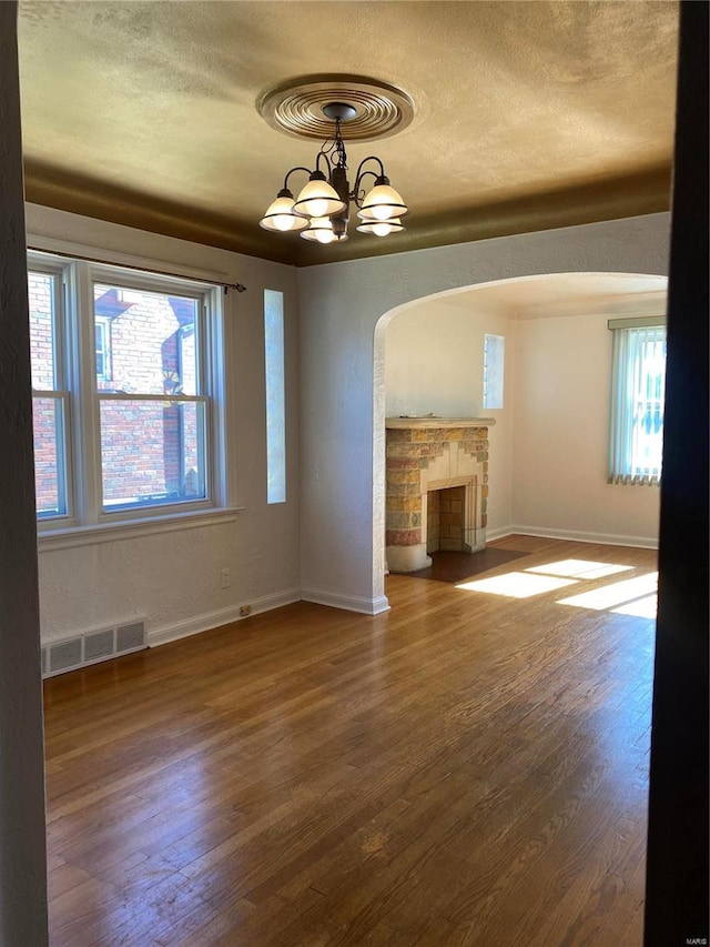 unfurnished living room with a fireplace, wood-type flooring, plenty of natural light, and a notable chandelier