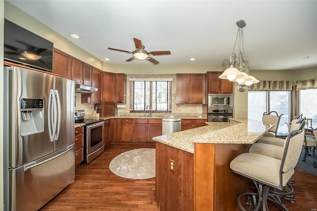 kitchen with light stone countertops, a center island, tasteful backsplash, pendant lighting, and appliances with stainless steel finishes