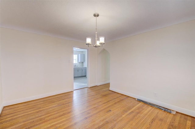 spare room featuring light wood-type flooring and a chandelier