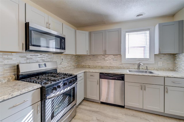 kitchen with sink, stainless steel appliances, tasteful backsplash, light hardwood / wood-style floors, and a textured ceiling