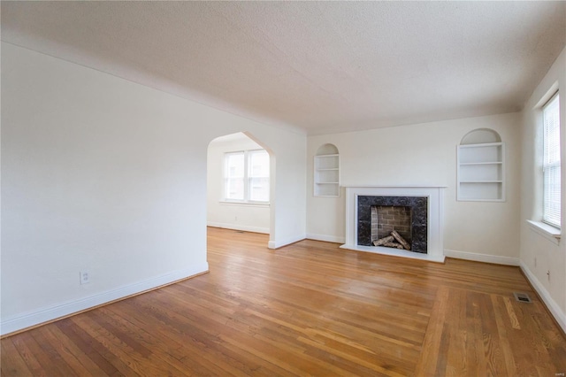 unfurnished living room featuring a textured ceiling, light hardwood / wood-style floors, and built in features