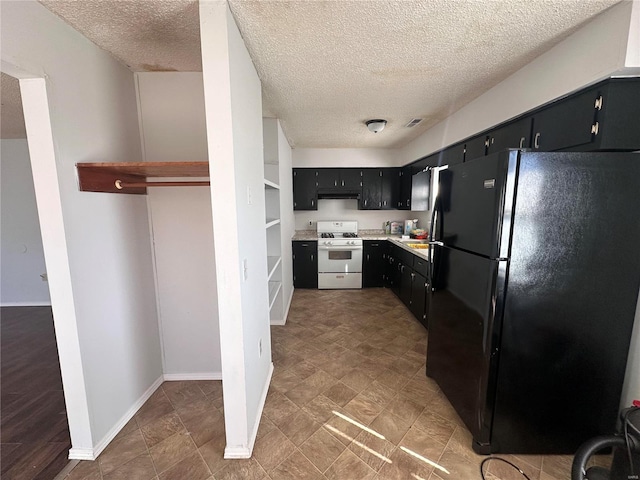 kitchen with white gas range oven, a textured ceiling, and black refrigerator