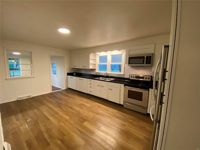 kitchen with white cabinets, tasteful backsplash, light hardwood / wood-style flooring, sink, and stainless steel appliances