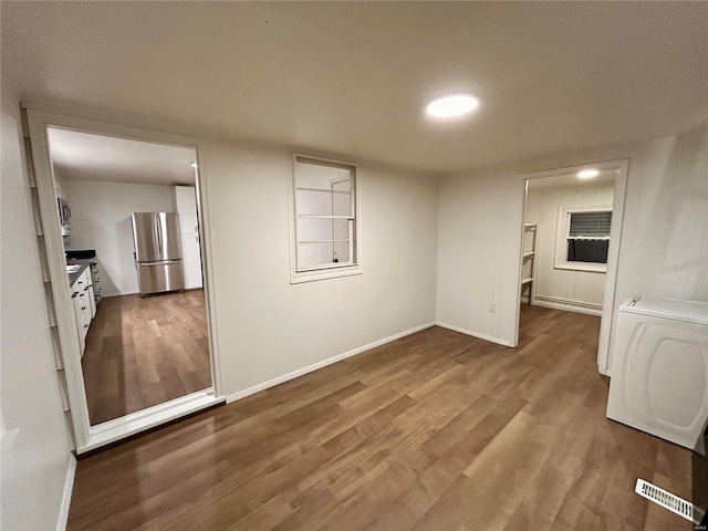 unfurnished room featuring washer / dryer, a baseboard heating unit, and hardwood / wood-style flooring