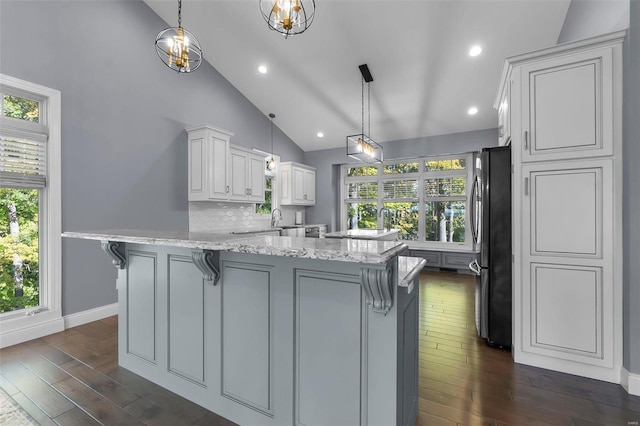 kitchen with white cabinets, light stone countertops, stainless steel refrigerator, dark wood-type flooring, and pendant lighting