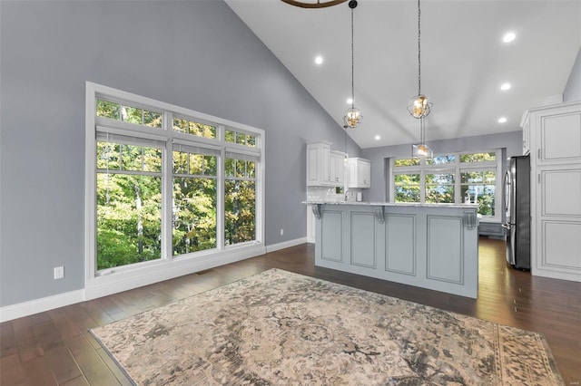 kitchen featuring a center island with sink, pendant lighting, white cabinetry, high vaulted ceiling, and stainless steel refrigerator