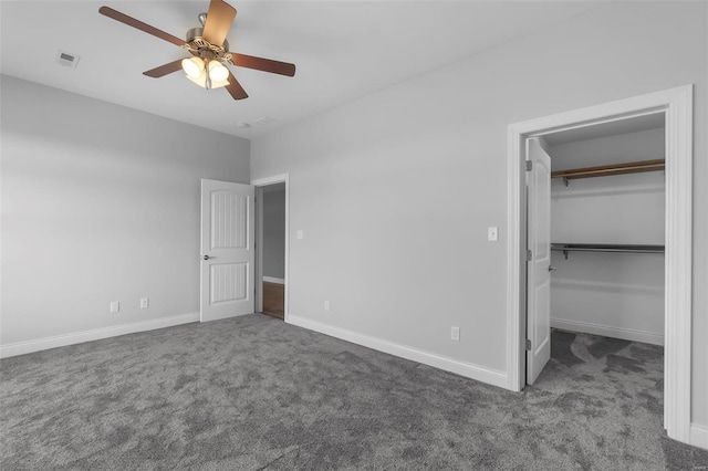 unfurnished bedroom with a spacious closet, dark colored carpet, a closet, and ceiling fan