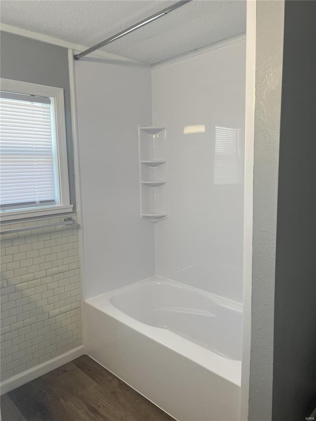 bathroom with washtub / shower combination, wood-type flooring, and a textured ceiling