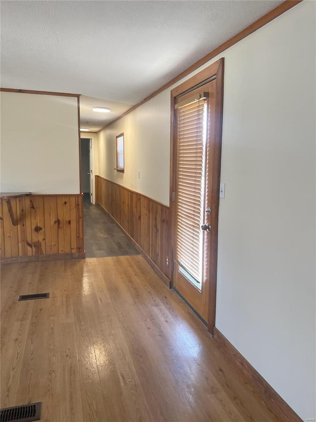 unfurnished room featuring a textured ceiling, crown molding, dark wood-type flooring, and wooden walls