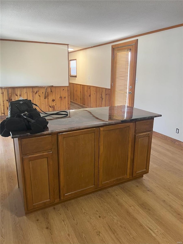 bar with wood walls, dark stone counters, light hardwood / wood-style floors, a textured ceiling, and ornamental molding