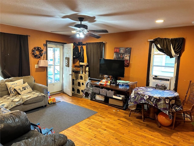 living room featuring ceiling fan, cooling unit, light hardwood / wood-style floors, and a textured ceiling