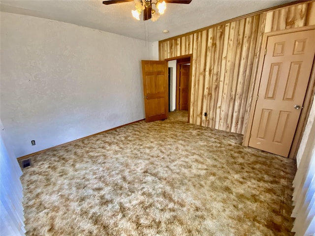 unfurnished bedroom featuring wood walls, a textured ceiling, carpet, and ceiling fan