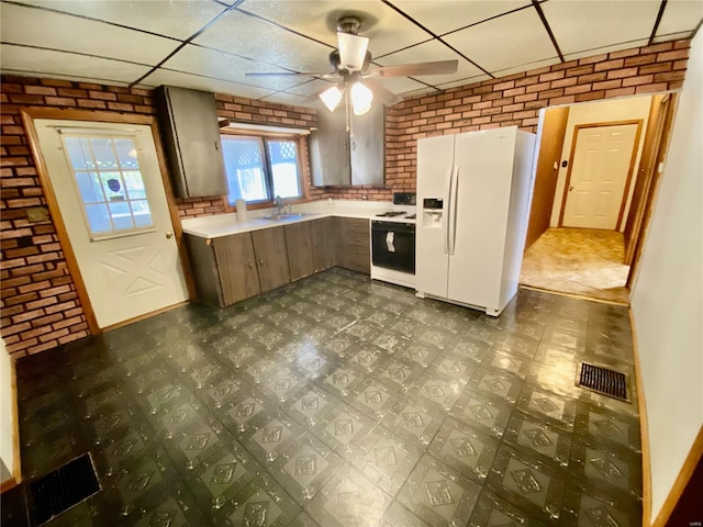 kitchen with ceiling fan, a paneled ceiling, sink, brick wall, and white appliances