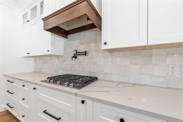 kitchen with custom exhaust hood, light stone countertops, stainless steel gas stovetop, white cabinetry, and backsplash