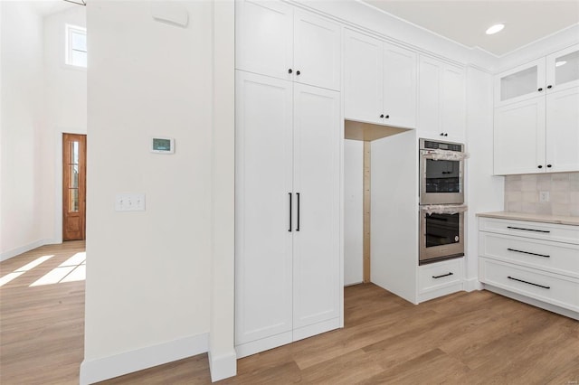 kitchen featuring white cabinets, stainless steel double oven, light wood-type flooring, and backsplash