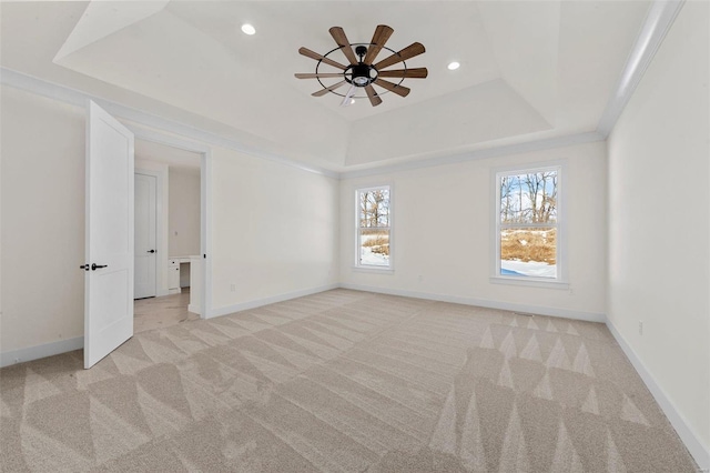 empty room featuring a raised ceiling, light carpet, ceiling fan, and ornamental molding