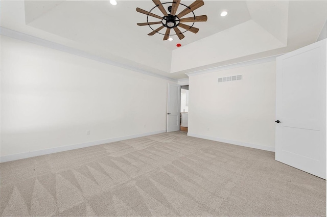 empty room with ceiling fan, a tray ceiling, and light colored carpet