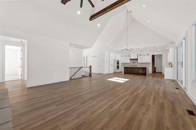 unfurnished living room with beam ceiling, dark wood-type flooring, high vaulted ceiling, and ceiling fan with notable chandelier