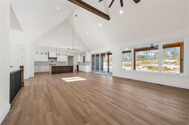 unfurnished living room with high vaulted ceiling, light hardwood / wood-style floors, plenty of natural light, and beam ceiling