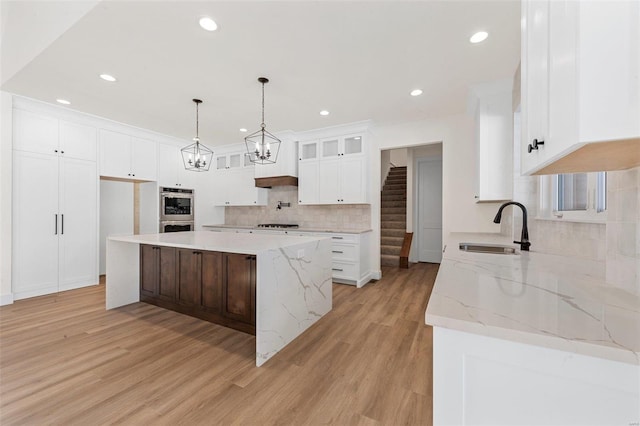 kitchen with a large island, double oven, white cabinets, light hardwood / wood-style flooring, and sink