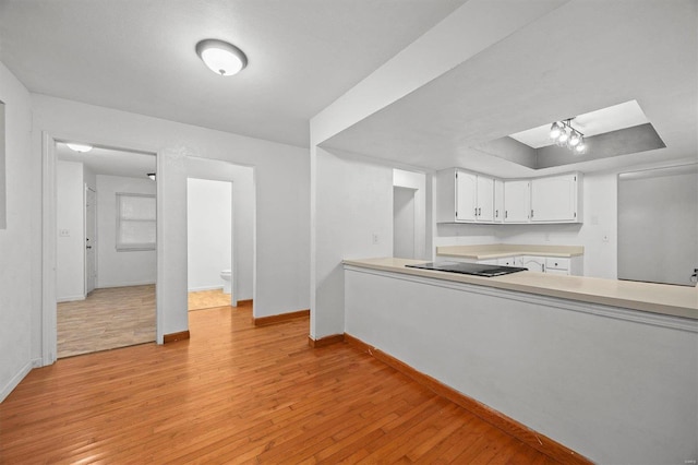 kitchen featuring white cabinets, a raised ceiling, light hardwood / wood-style floors, and black electric cooktop