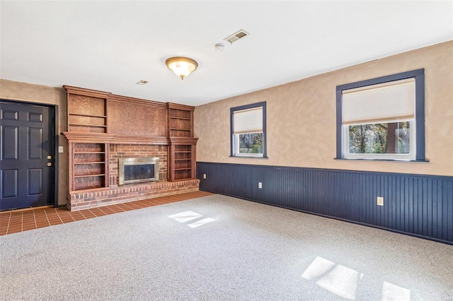 unfurnished living room with built in shelves, wooden walls, a fireplace, and carpet