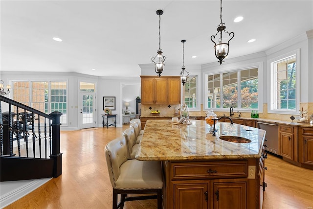 kitchen featuring decorative backsplash, stainless steel dishwasher, a kitchen island with sink, a healthy amount of sunlight, and sink