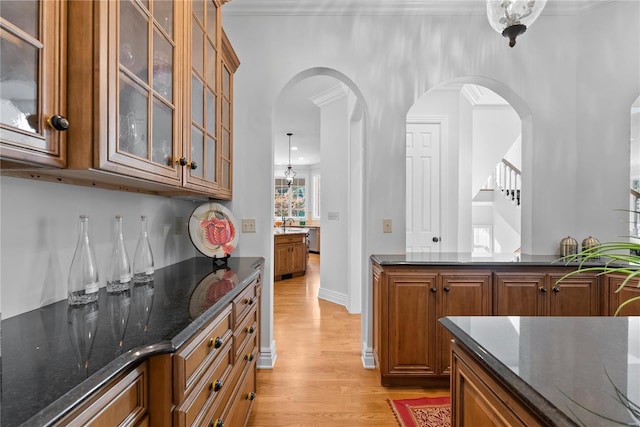 bar with light wood-type flooring, dark stone counters, crown molding, sink, and hanging light fixtures