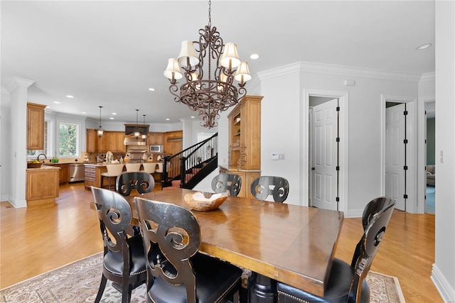 dining space featuring sink, an inviting chandelier, light hardwood / wood-style flooring, decorative columns, and crown molding