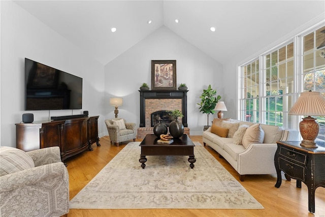 living room featuring a brick fireplace, vaulted ceiling, and light hardwood / wood-style flooring