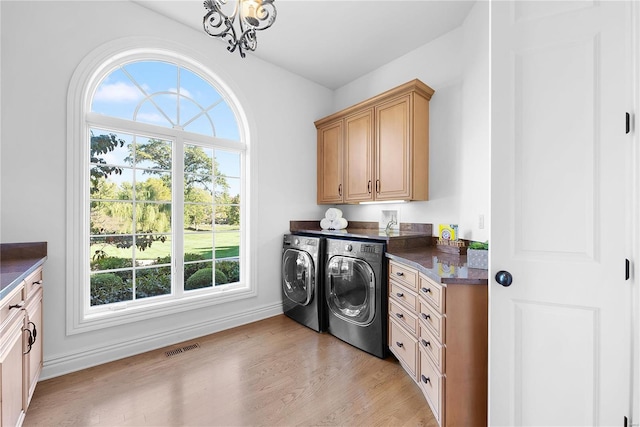 clothes washing area featuring a healthy amount of sunlight, washer and dryer, cabinets, and light hardwood / wood-style floors